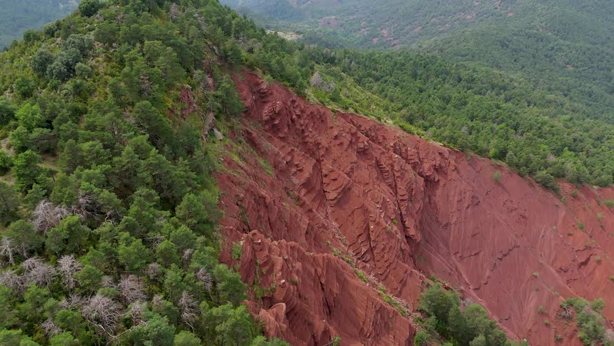 Mountain slope with reddish rock cliff surrounded by dense vegetation
