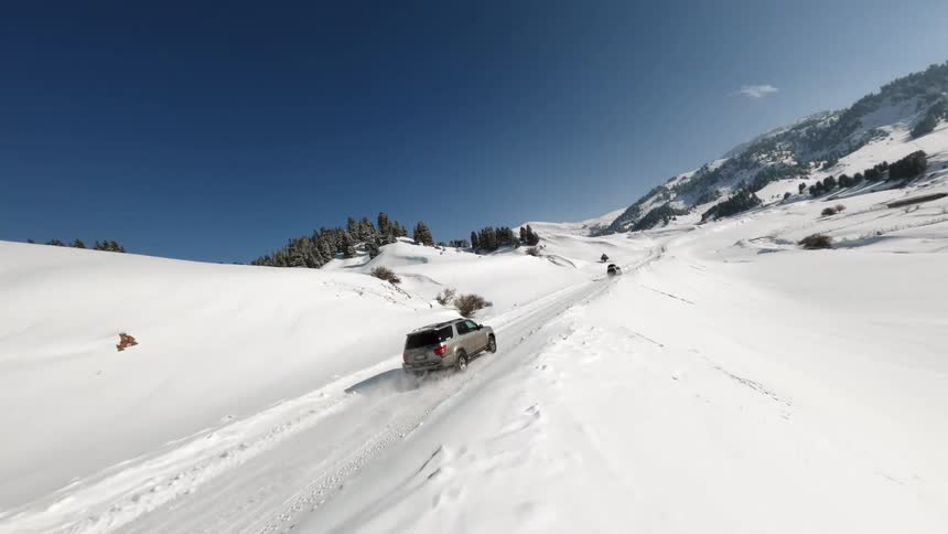 Suv drives along snowy trail in mountainous landscape under clear sky