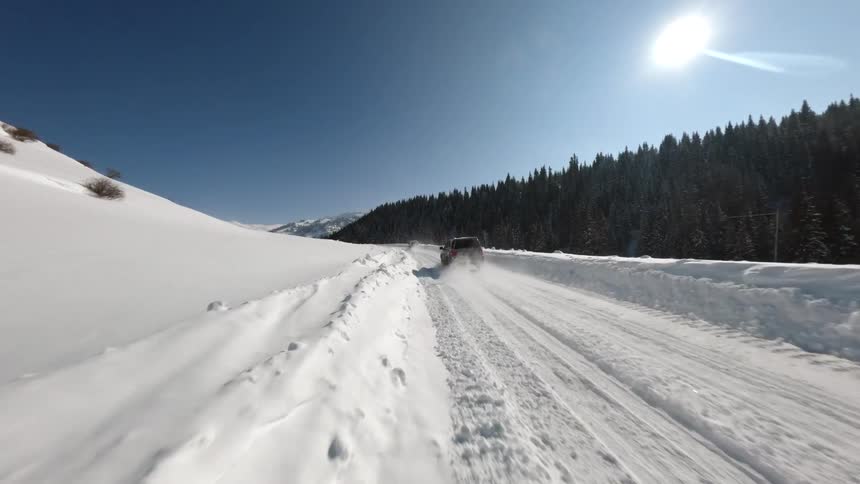A narrow road carved through deep snow in a vast mountain valley under a bright sun