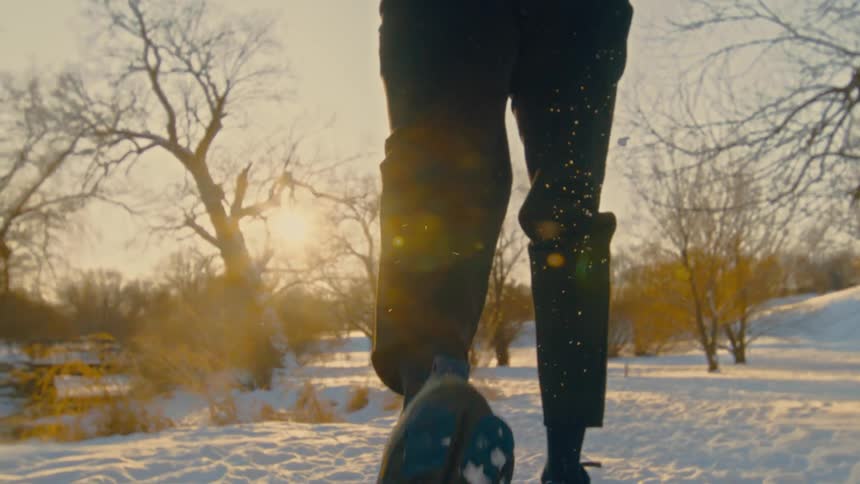 A person runs away from the camera on a snow covered trail during a bright sunset