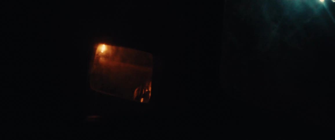 Side mirror of a vehicle driving through the woods at night reflects the headlights of another vehicle