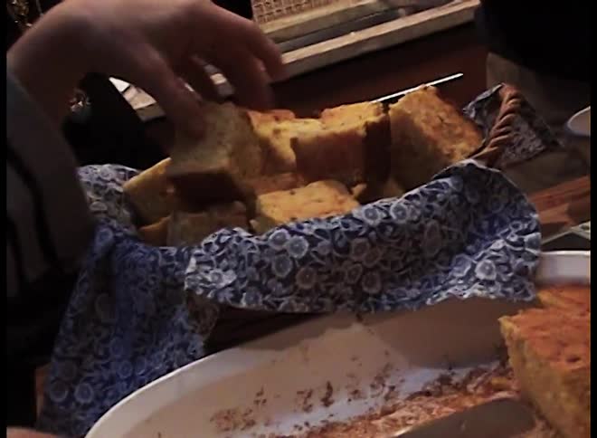 Woman cubes cornbread while her family moves around her in the kitchen