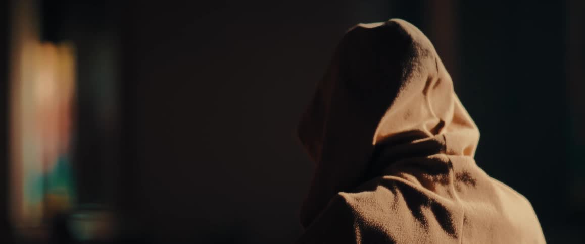 A person wearing a tan hooded sweatshirt sits with the back to the camera in a church