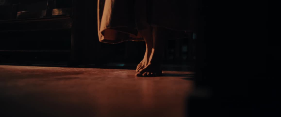 Barefoot person wearing a cloak kneels next to a pew