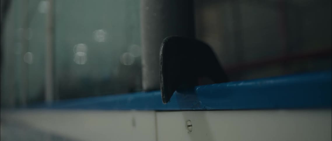 A black hockey stick blade leaning against blue arena boards