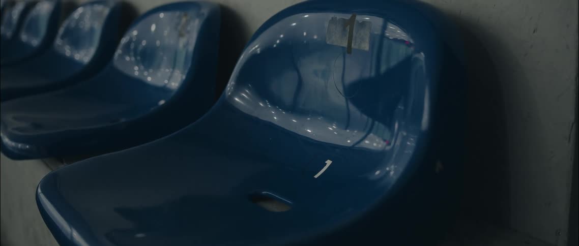 Row of blue plastic stadium seats with white stickers numbered one in dark arena