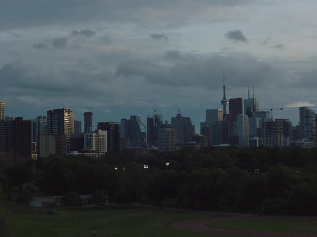 Buildings and towers on the city skyline as trees bend in the wind and clouds move across the sky