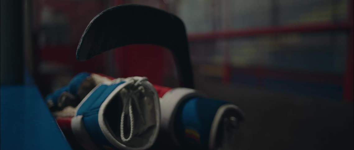 Blue and red hockey glove resting on a bench with a stick in the background
