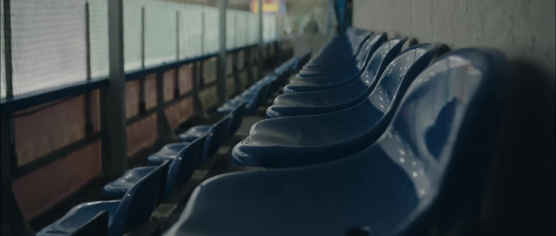 Rows of empty blue seats beside an ice rink enclosed by netting
