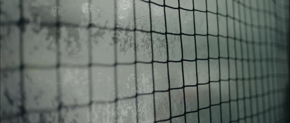 A closeup shot focuses on a safety net while behind it the frosted and wet plexiglass of an ice rink obscures the view of the action