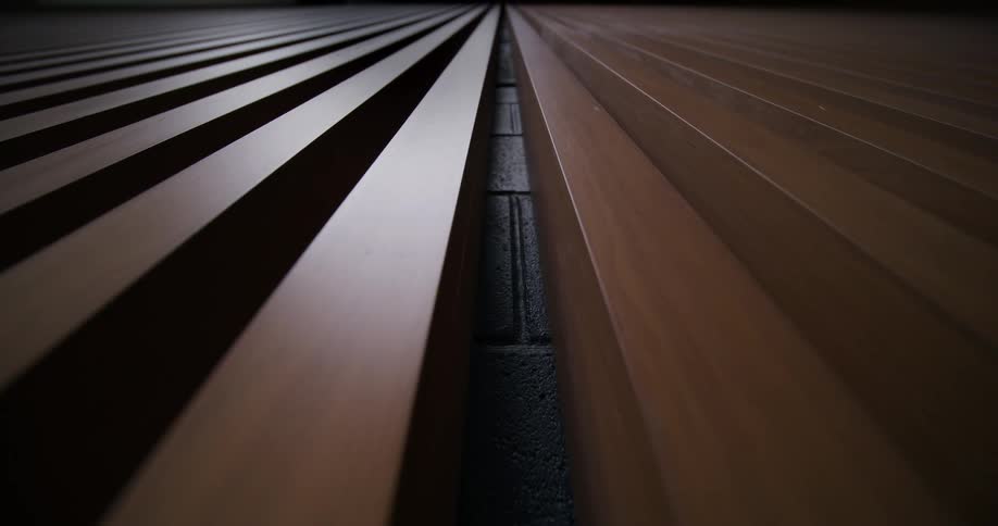 Two parallel structures made of vertical slats separated by a dark gap that reveals a textured surface
