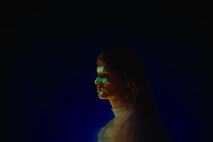 A young woman stands in a dark room with text projected onto her face