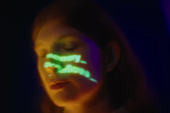 Womans face illuminated by a colorful projection with highlighted text across her skin