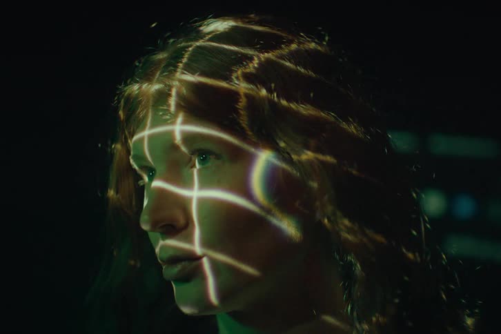 Abstract light patterns are projected onto a womans face and hair in a dark setting