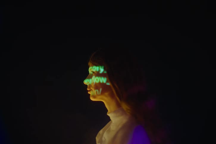 Woman in a dark environment with green glowing text projected on her face