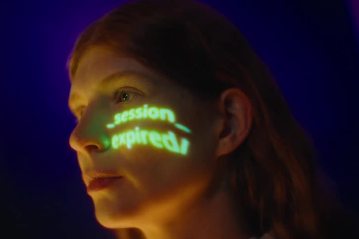 Glowing green text cycles through phrases like memory overflow and session expired projected directly onto the womans face in a dark setting