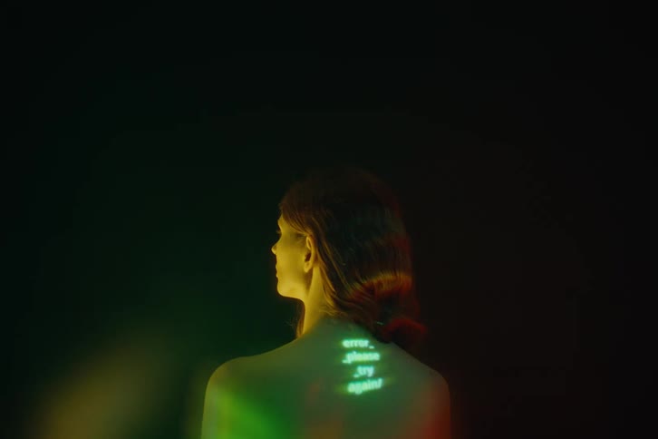 Projected words appear on the back of a redheaded woman standing in a shadowed area
