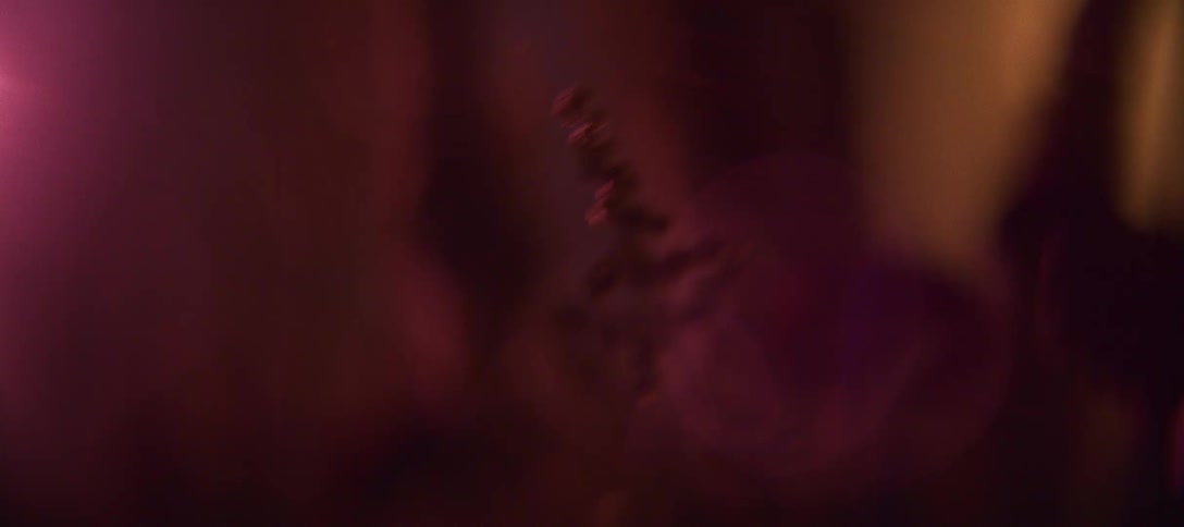 A closeup shot in dim red lighting and a hand holding fire and a small round object with a chain or beaded detail hanging beside it