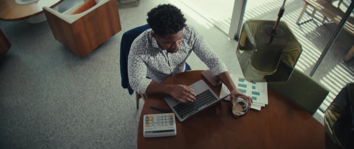 Man drinks water while typing on a laptop at home