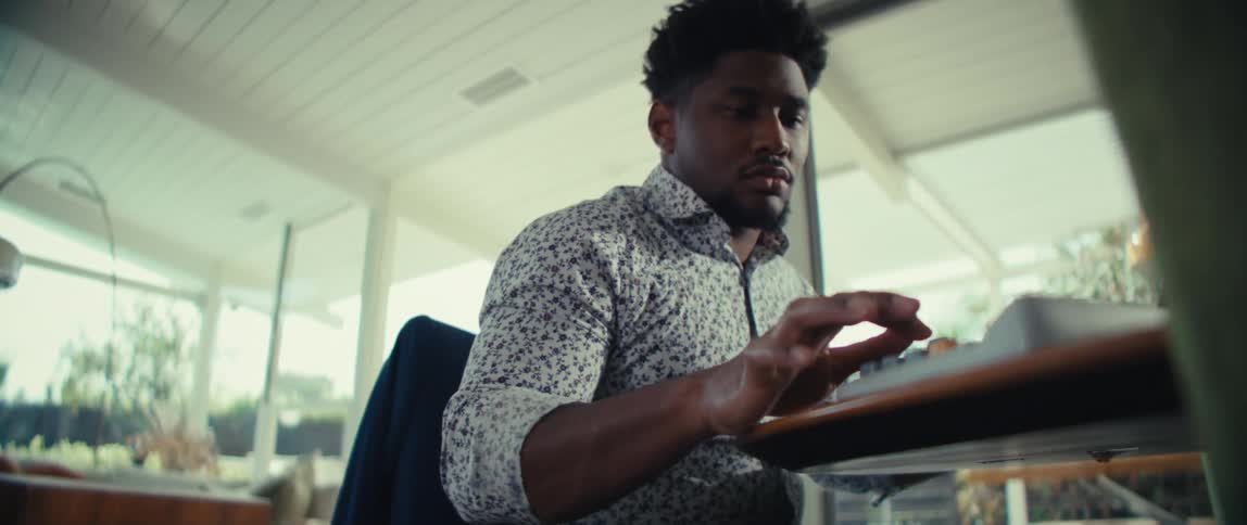 A black male office worker sits behind a desk inside an office typing on a keyboard at midday