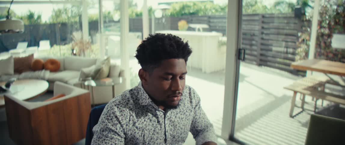 A man works on a laptop at a table inside a modern home