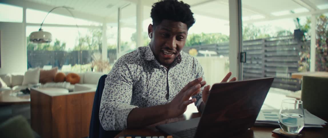 Man sitting at a table typing on a laptop computer as he moves his hands smiling and laughing