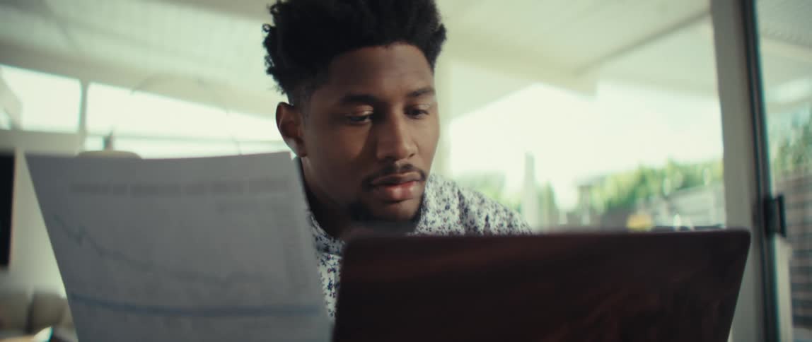 Man sitting at a table in front of a laptop computer as he reads a document