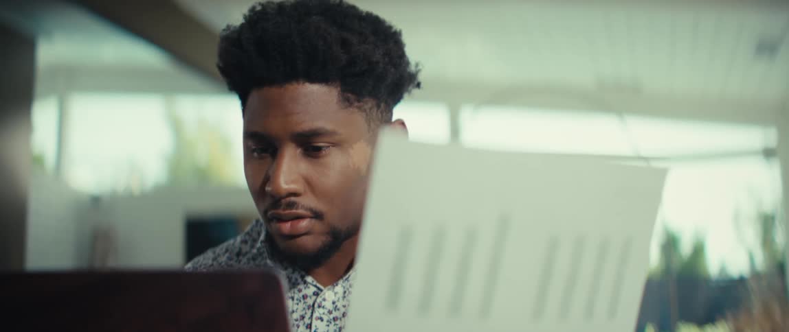 The man holds the paper up to the laptop