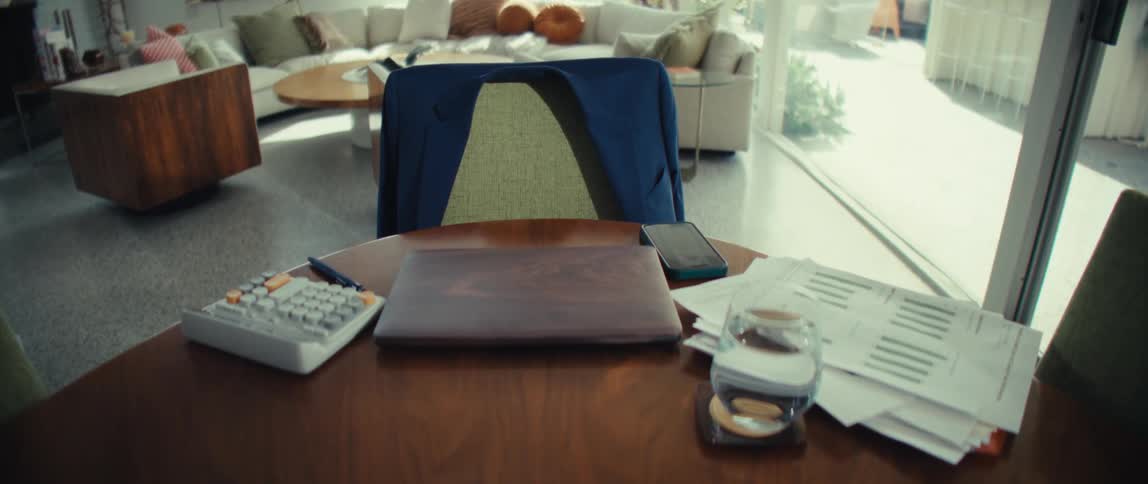 Table with closed laptop calculator smartphone documents and a glass of water in a bright room with no people