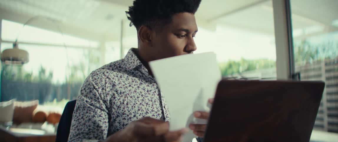Man sitting at a table in front of a laptop computer as he looks at paperwork