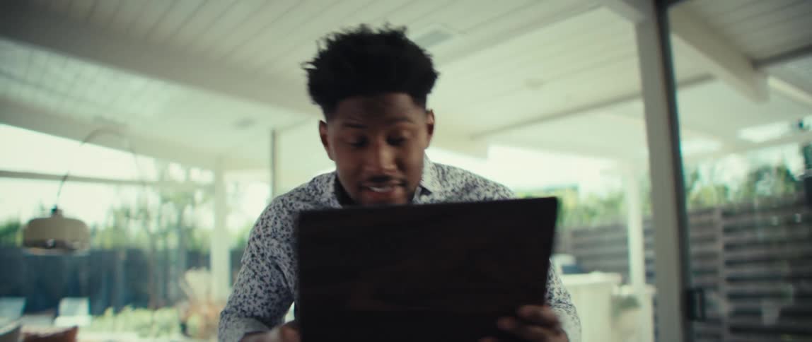 Man leaning forward holding an open laptop with a surprised expression in a bright residential setting