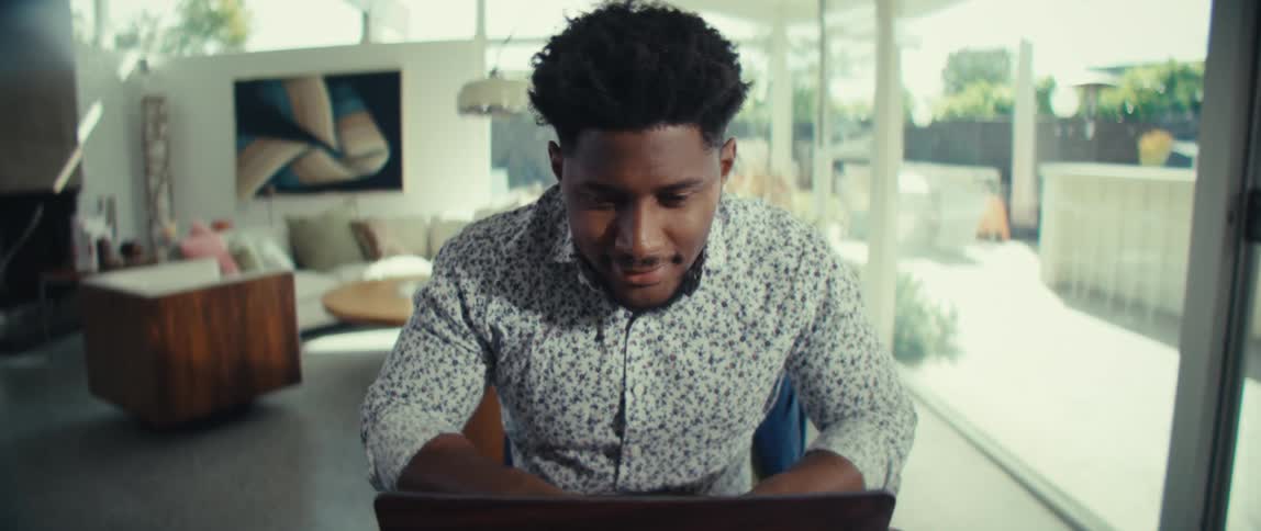 Man seated at a table reviewing a printed document with a laptop calculator and a glass of water in a bright room