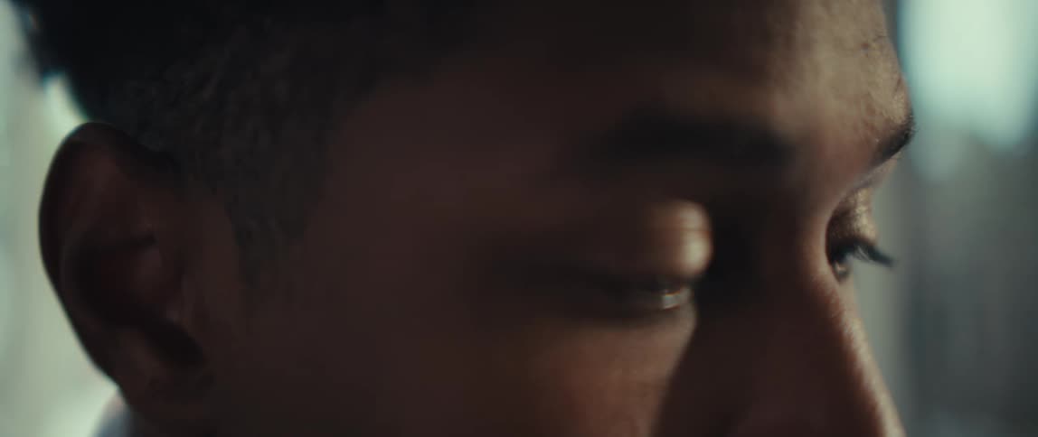 A close view of a man looking down while his eyes move as if reading or working in a bright indoor setting
