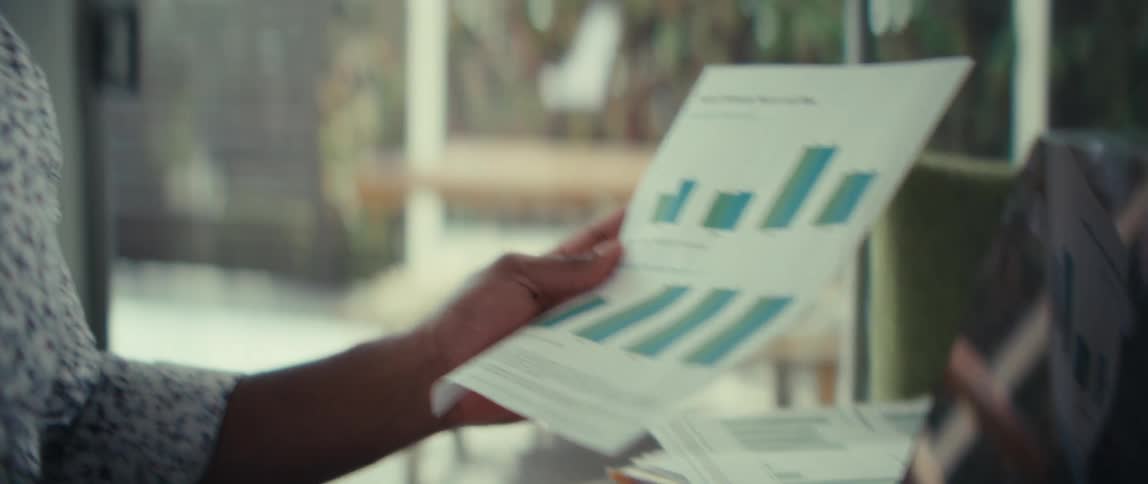 Person holding a report with a bar chart while pointing at a laptop screen
