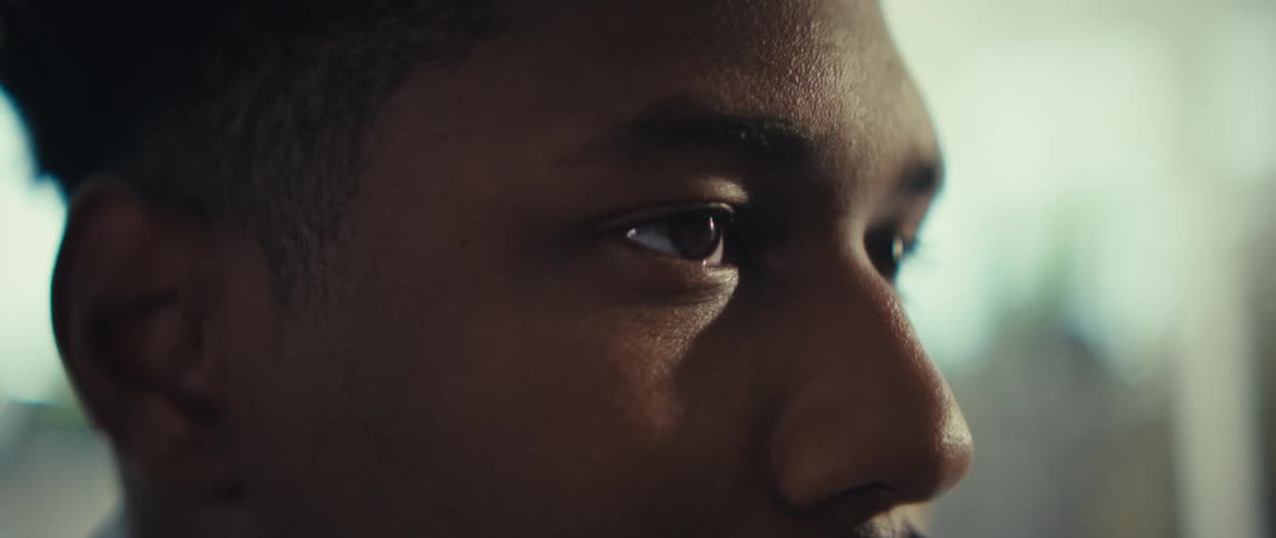 A close up side profile of a young man with dark skin and short hair as he looks forward and blinks his eyes while soft natural light illuminates his face