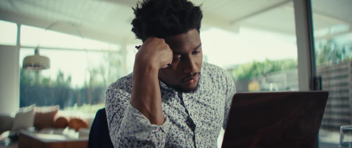 Man using a laptop and calculator at a table in a bright residential setting