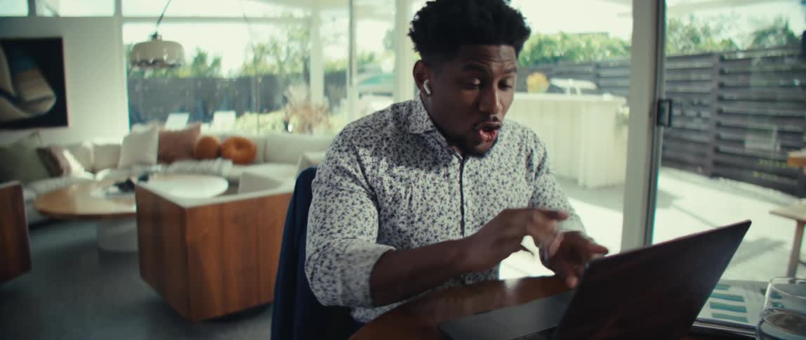 Man sitting at a table having a conversation on a laptop computer moving his hands as he talks