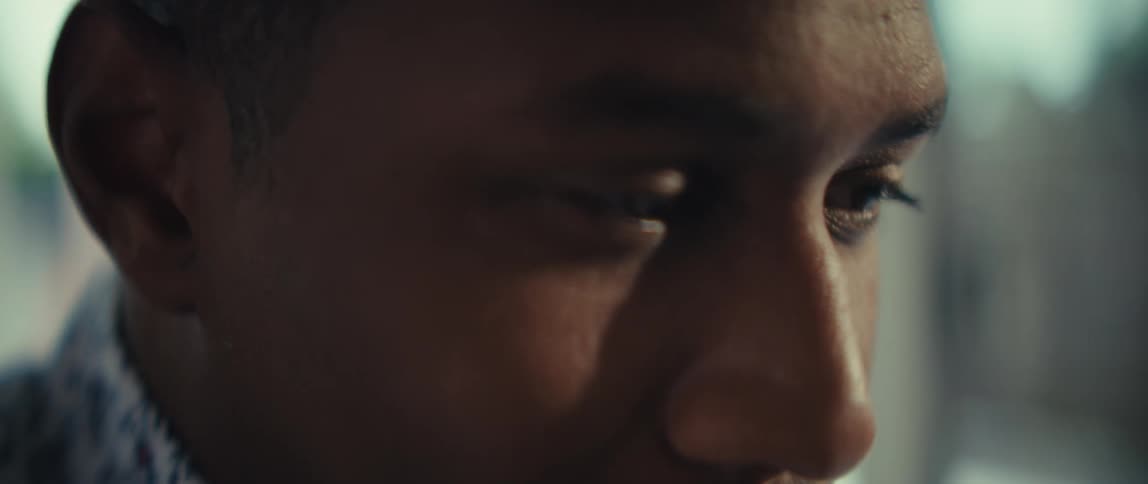 A blurred a closeup shows a persons hands moving over a keyboard then moving up to show his facein a softly lit setting