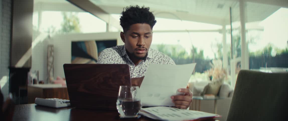 Man reviewing a document and using a calculator beside a laptop in a bright room