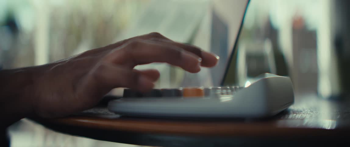 A persons hand is shown typing on a calculator while reviewing printed bar charts and financial documents the scene is shot with a shallow depth of field focusing on the rhythmic movement of the fingers against the calculator keys