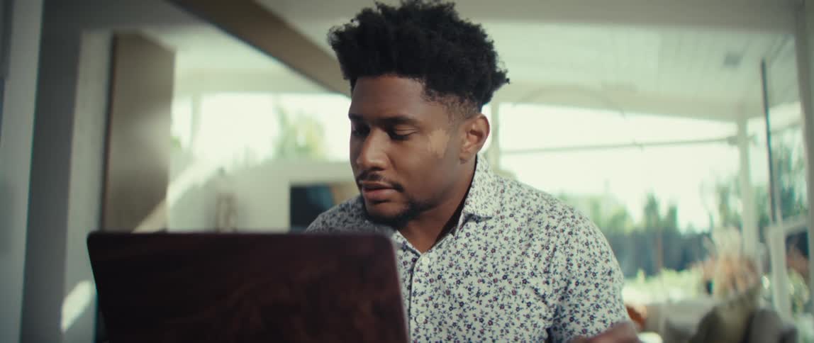 Man sitting at a table in front of a laptop computer reading a document and pressing keys on the calculator and rubbing his face with his hand