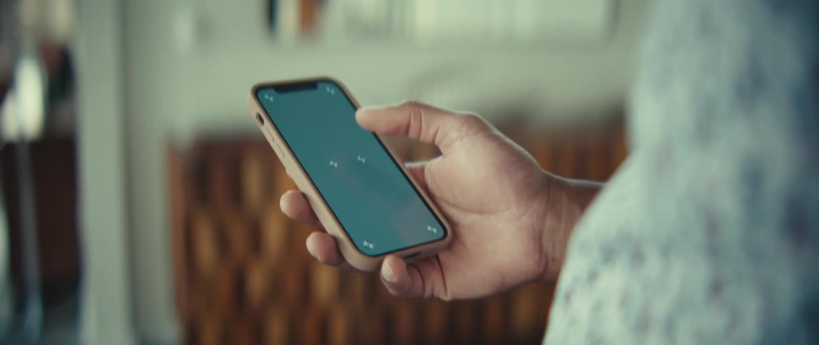A person holds a smartphone and scrolls through it indoors at midday