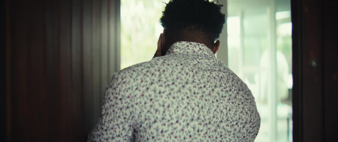 Young adult black man talking on a smartphone while going through a wooden door during day time