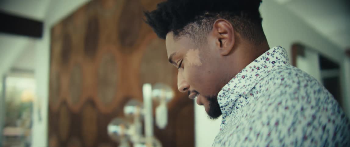 A black man with a floral shirt walks through a modern house while talking on his mobile phone
