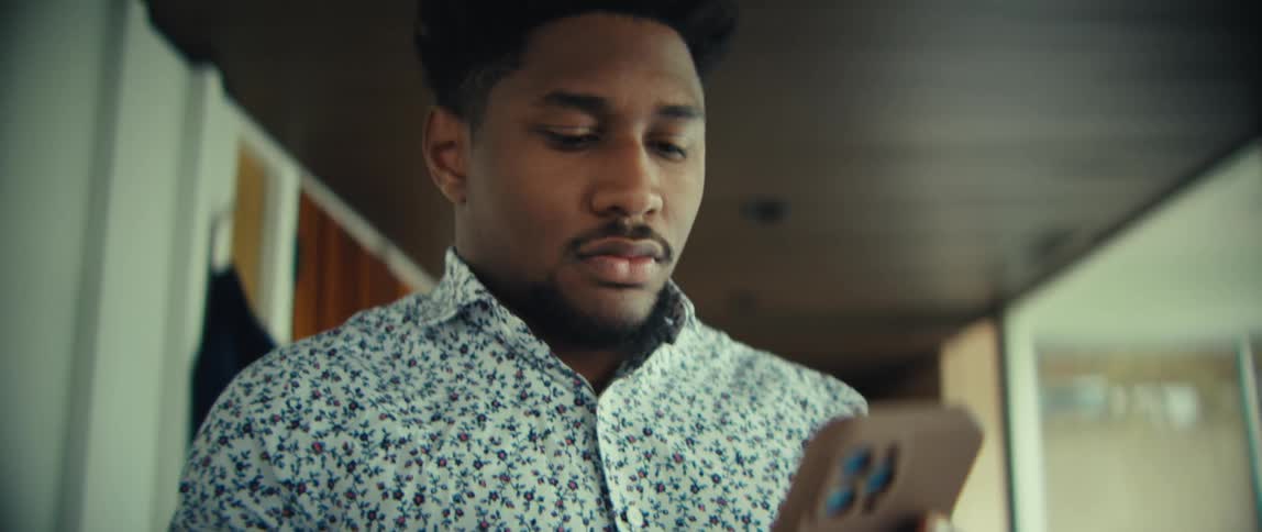 Young adult black man walking indoors and texting on a smartphone with a nervous facial expression during day time