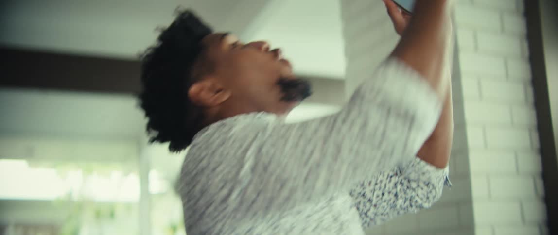 Young adult black man talking in front of a smartphone held in his hand then smiling and cheering indoors during day time