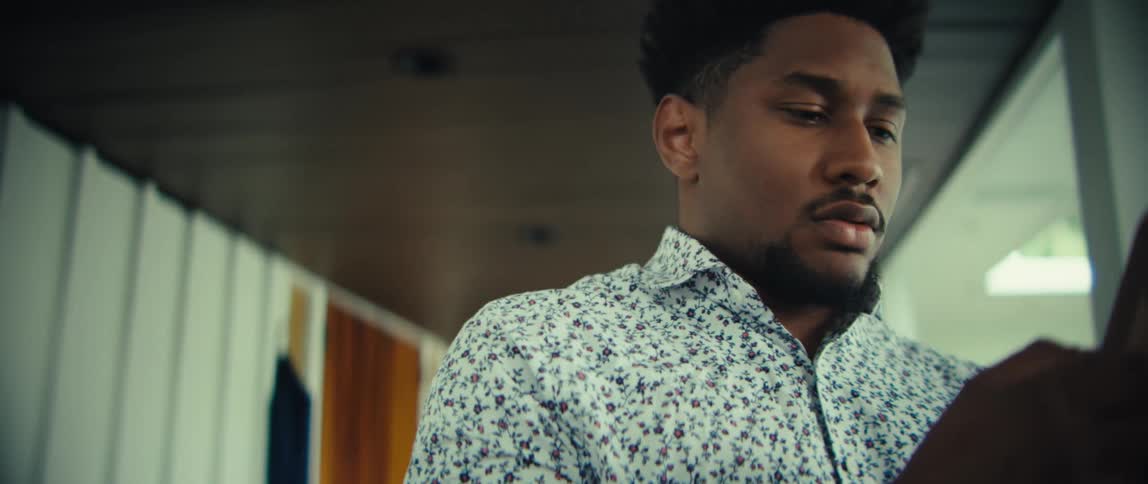 A man wearing a floral patterned shirt looks at his phone and smiles within a bright modern indoor setting