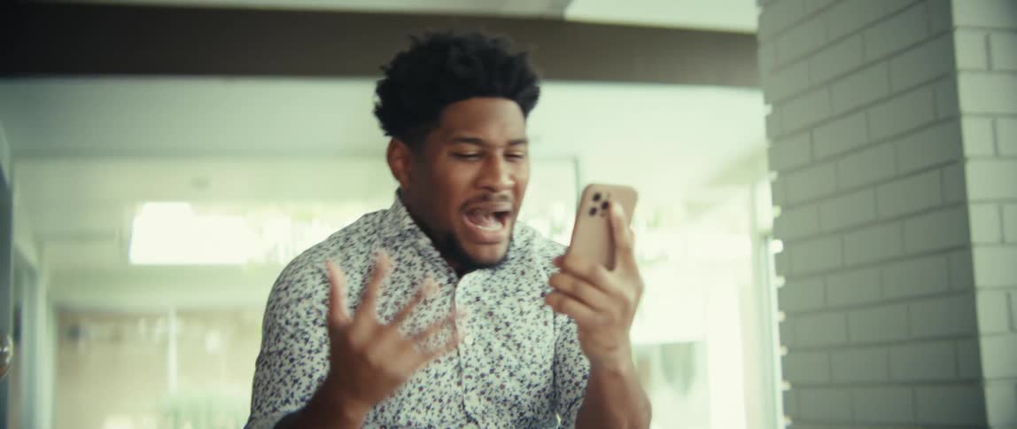 Man is excited as he walks through a room talking on his phone raising his hands in celebration