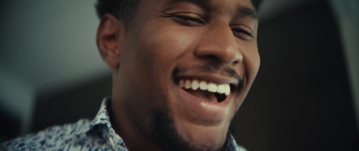Young adult black man smiling and laughing while holding a smartphone on his hand indoors during day time