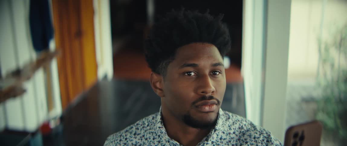 A man walks toward the camera while looking down at his smartphonehe pauses briefly to glance forward with a neutral expression before moving out of the frame